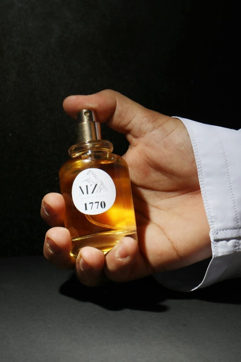 Close-up of a hand holding a perfume bottle with shadowed backdrop, emphasizing elegance.